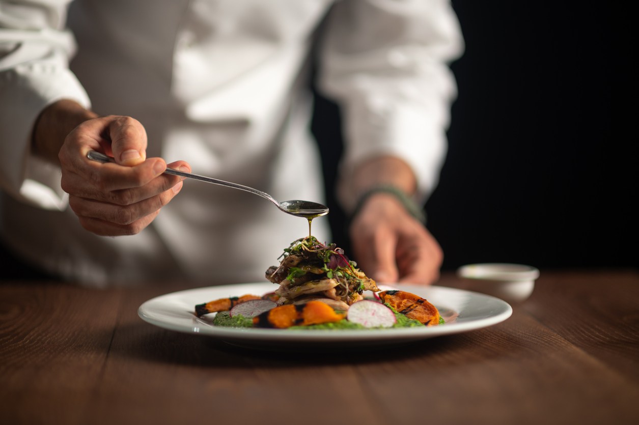 A male chef pouring sauce on meal A male chef pouring sauce from the spoon on meal on a black background.